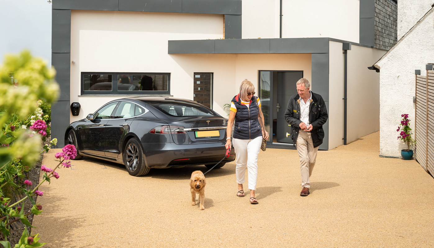 Two people in front of their house walking their dog. The image showcases Oltco's resin driveways.